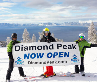 three skiers holding now open sign
